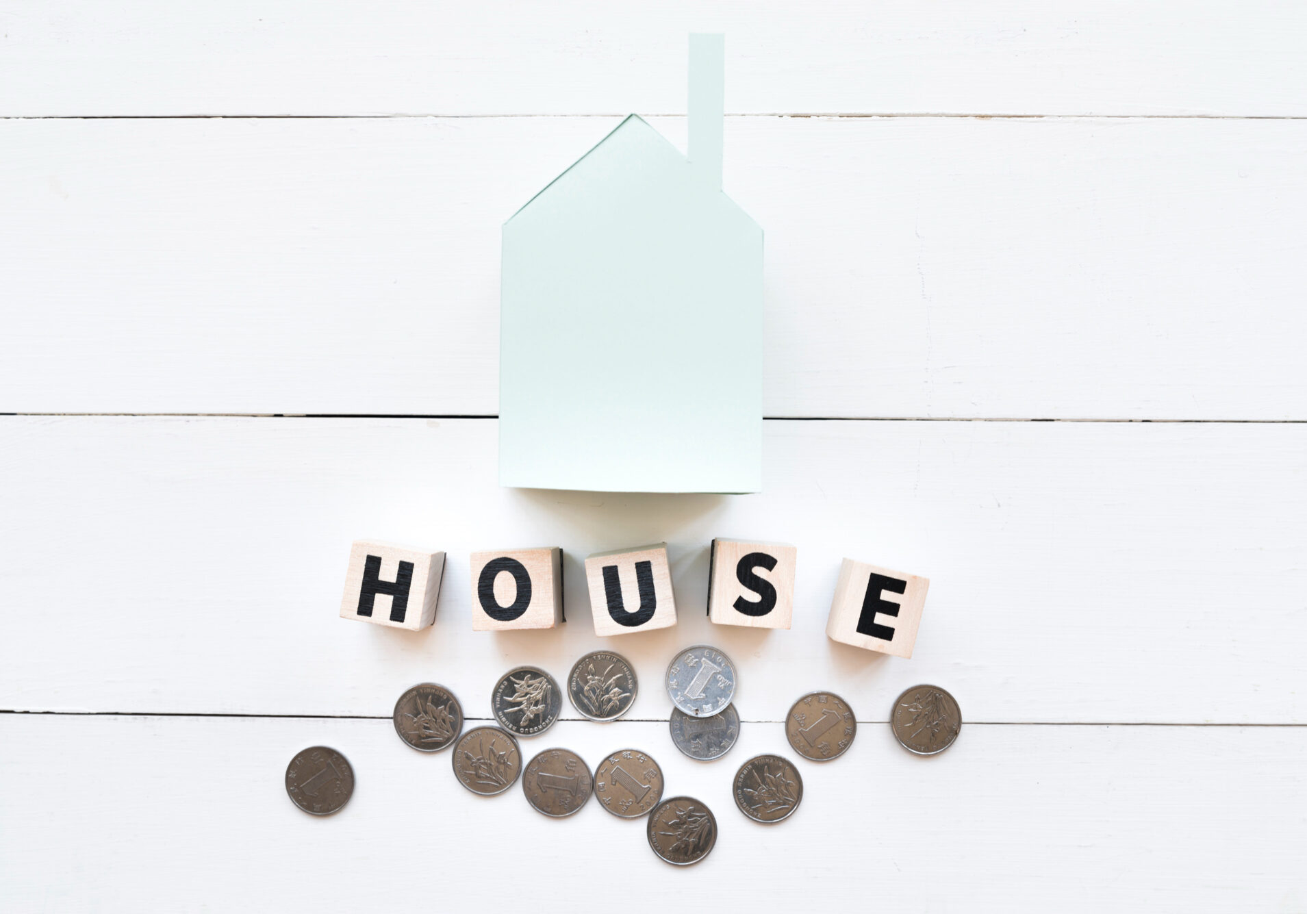 blue-paper-house-model-with-wooden-blocks-coins-white-wooden-backdrop