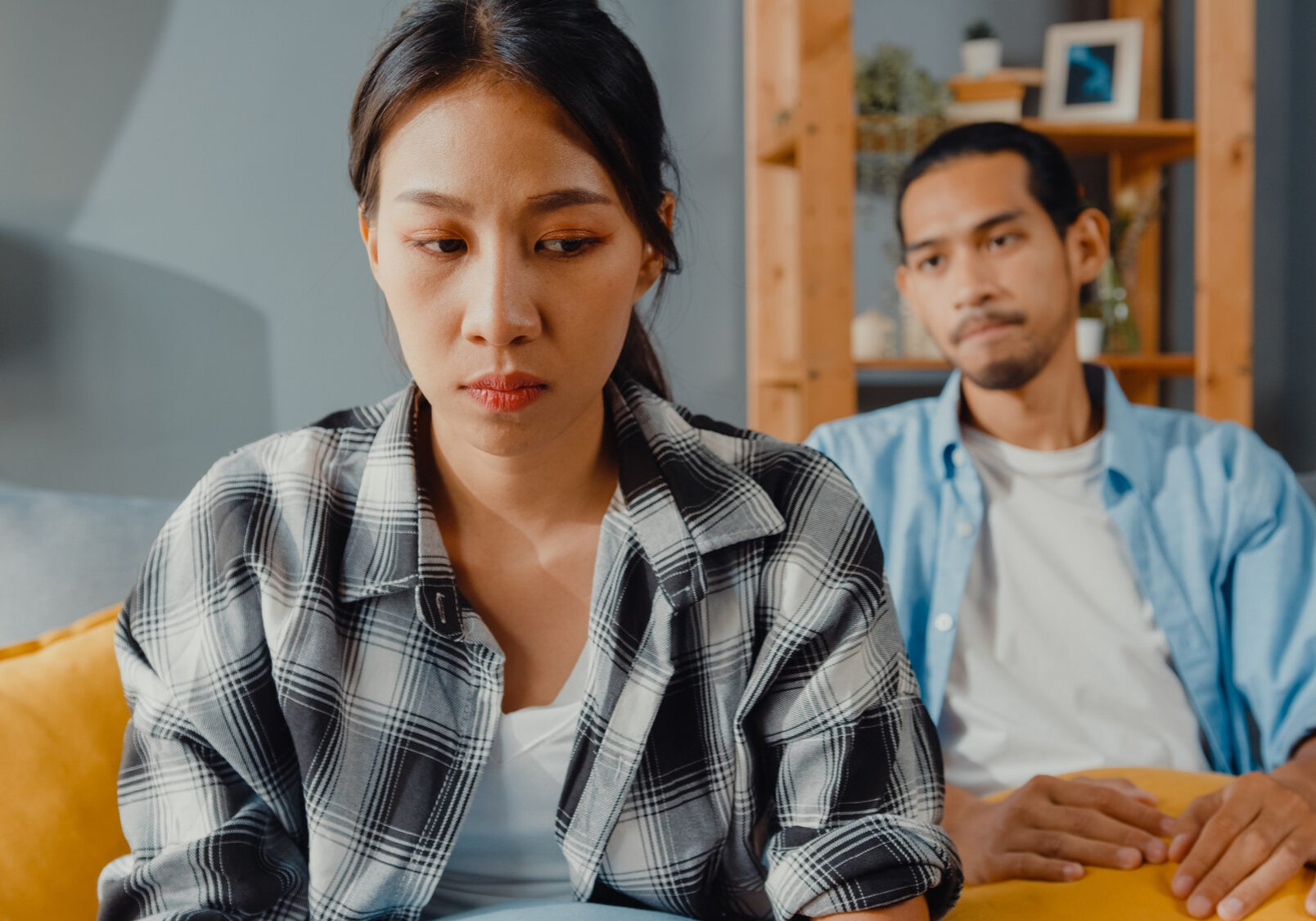 upset-asian-couple-sit-couch-living-room